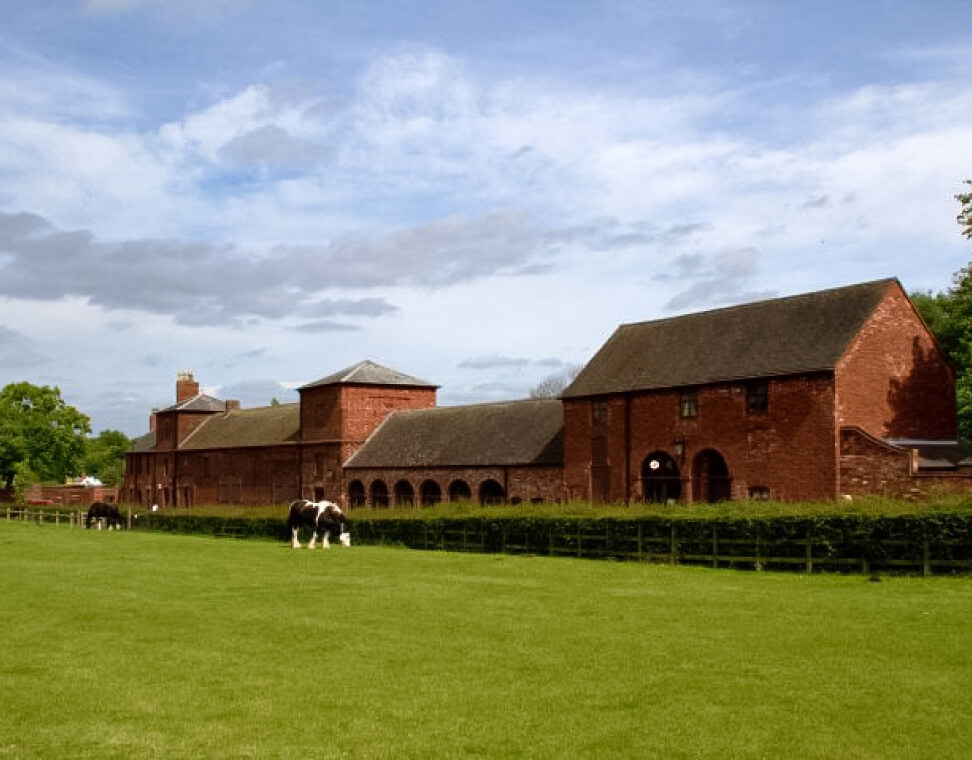 Image depicts a building set in a lush green surrounding with animals grazing Infront of it