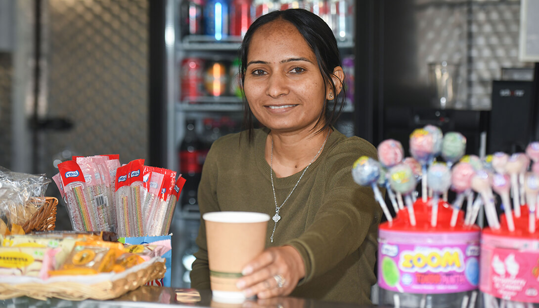 A lady putting forward a glass of cool drink in a shop at Sandwell valley where different kinds of sweets and drinks are displayed